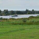 Rural Transport - a boat traveling down a river next to a lush green field