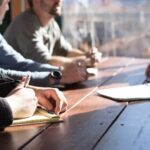 Collaboration Handshake - people sitting on chair in front of table while holding pens during daytime