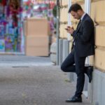Lean Thinking - man holding his phone while leaning on building