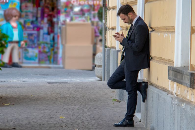 Lean Thinking - man holding his phone while leaning on building