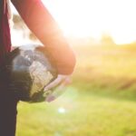 Global Expansion - person holding black and brown globe ball while standing on grass land golden hour photography